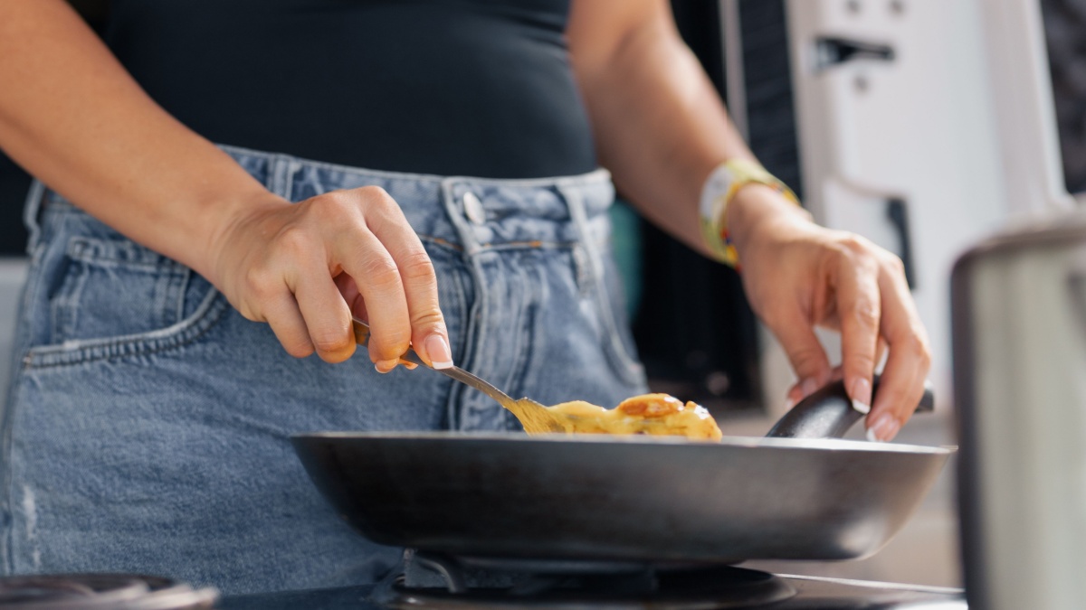 Young attractive woman cooking scramble eggs in the beach..