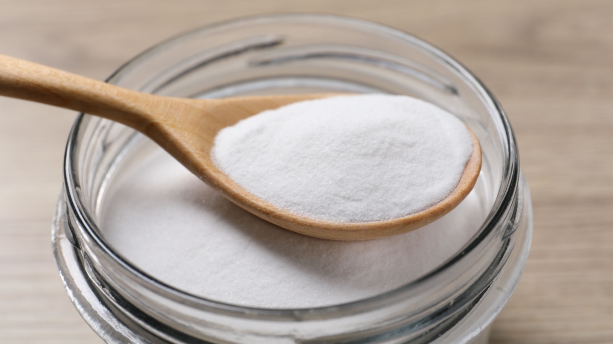 Baking soda in glass jar on wooden table, closeup.