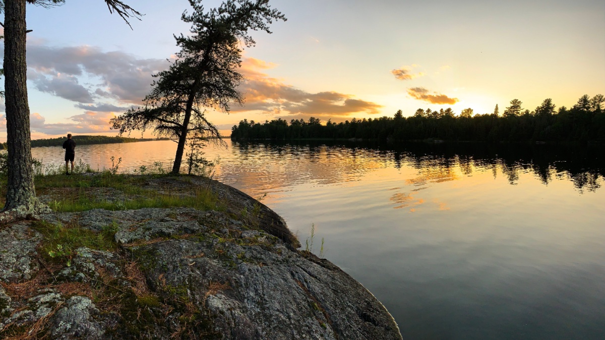 A man watches sunset from a round rock outcrop over a lake. Voyageurs National Park, Minnesota.