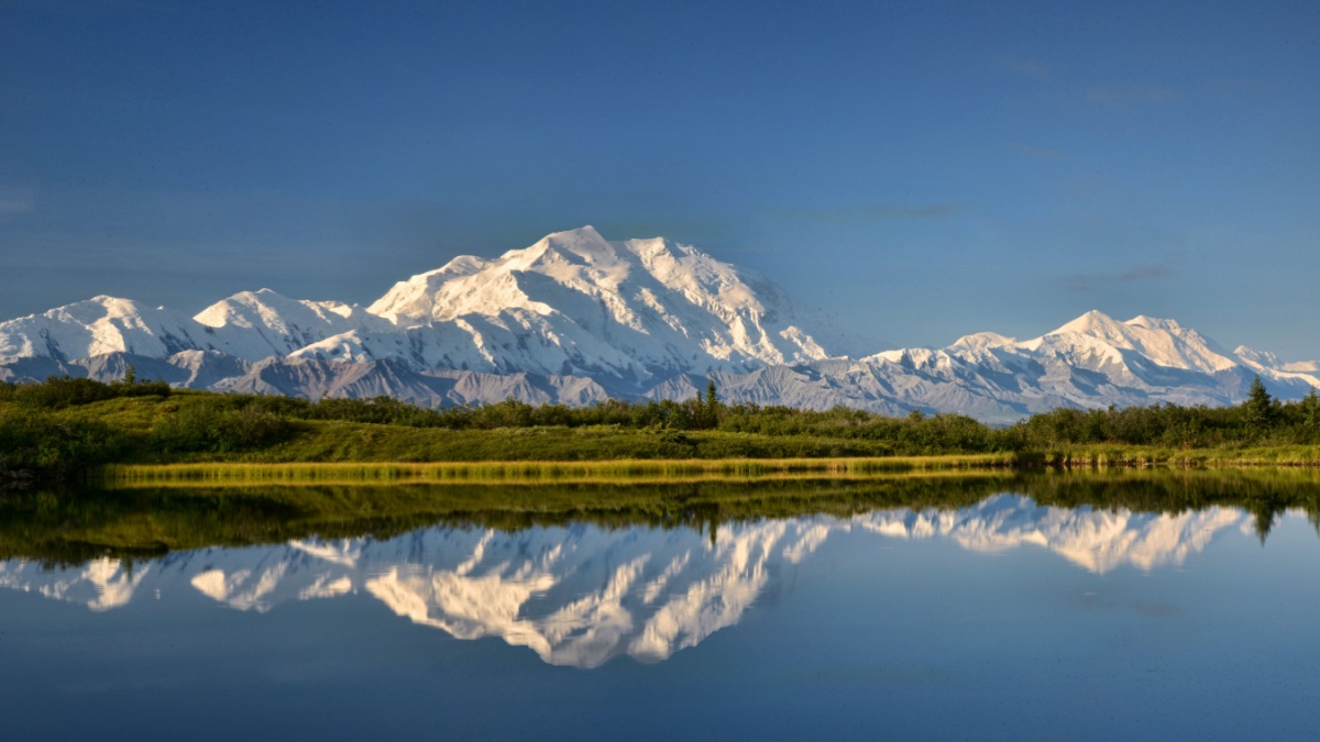 view of alaska's mount denali reflected in calm Reflecting Pond near Wonder Lake, with clear blue sky above.