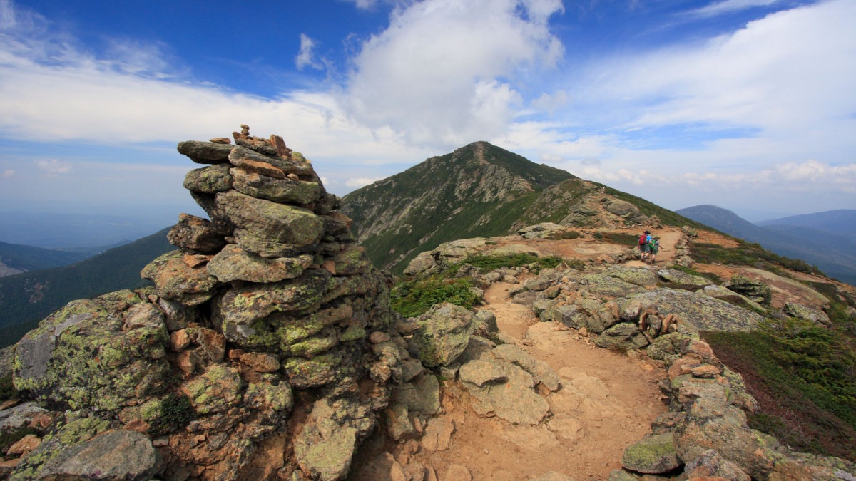 Hikers trekking along Franconia mountain ridge traverse, with a beautiful landscape background and blue sky. Mount Lafayette, Mount Lincoln, New Hampshire, USA.