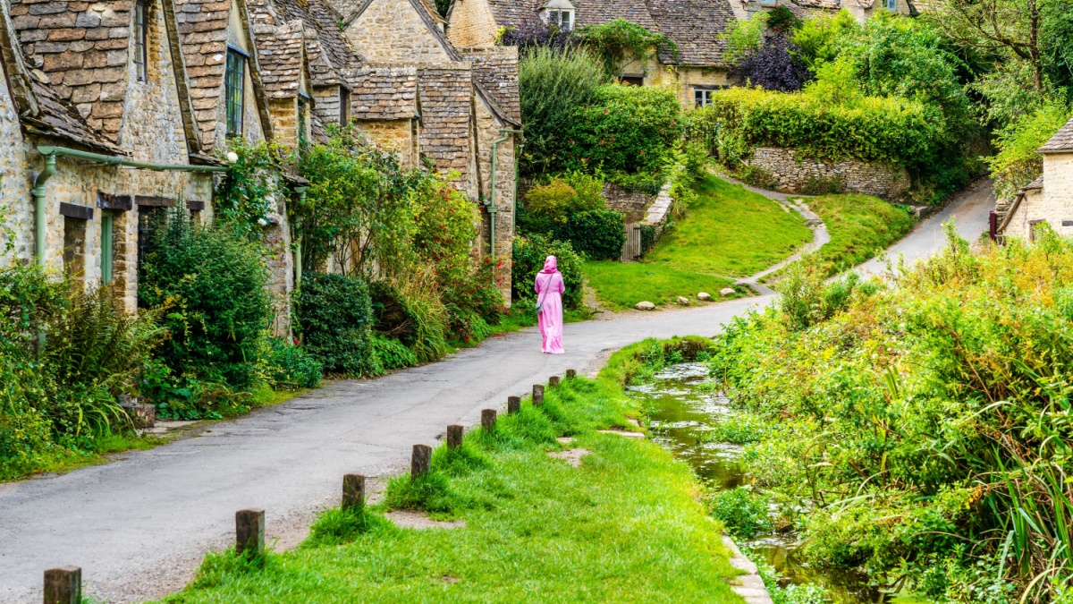 Walking down the path along the traditional row of stone cottage houses on Arlington Row in Bibury village, Gloucestershire, The Cotswolds, England UK.