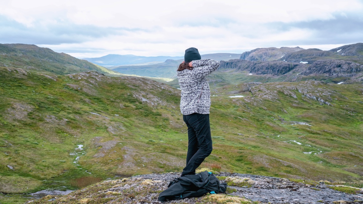 Mature woman adjusts warmer clothes, hiking at high altitude cold Norwegian Mountains range terrain. Hiking high in Norwegian mountains. Norway, Krutvatnet. Side view.