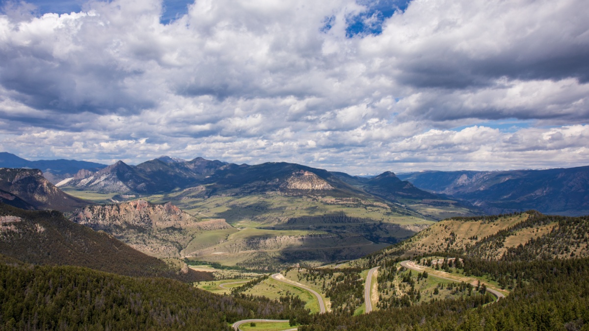 View from the top of Dead Indian Pass in Wyoming. Chief Joseph Byway in northwest Wyoming. Green landscape with blue sky and puffy white clouds. Switchback highway on horizon.