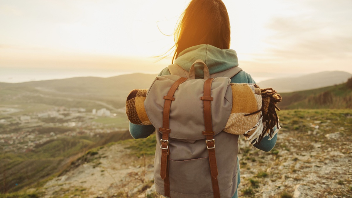 Hiker woman with backpack and sleeping bag walking in the mountains in summer at sunset.