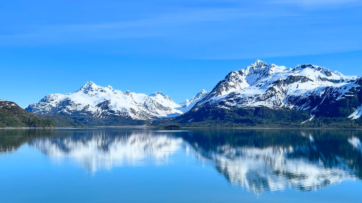 Snow capped mountains reflect off a calm ocean in Glacier Bay National Park, Alaska.
