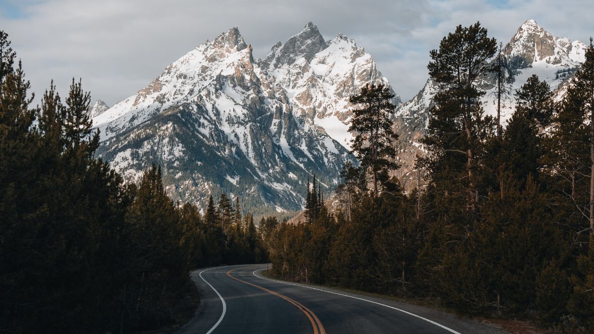 A winding paved road to Grand Targhee ski area looks up toward the summit of the Grand Teton in Wyoming.
