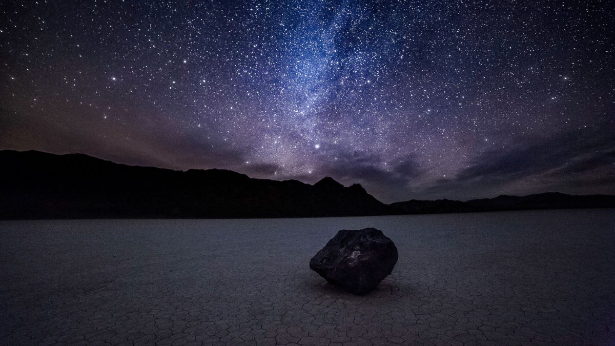 Night sky and the milky way over a moving rock at the Racetrack in Death Valley National Park in California.