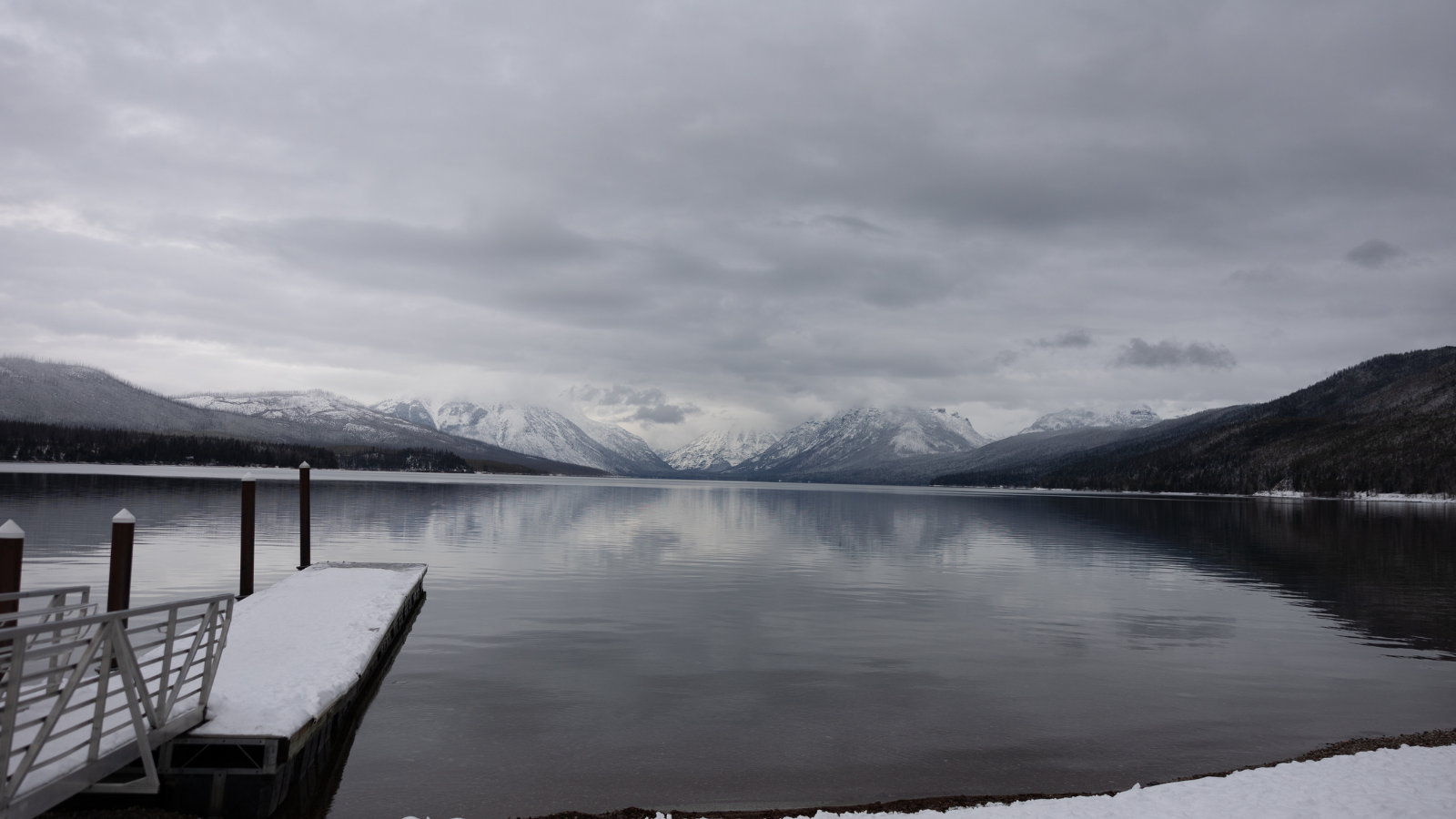 Montana lake McDonald in the national glacier park during winter with snow. Clear blue ice water with colorful stones with beautiful reflection.