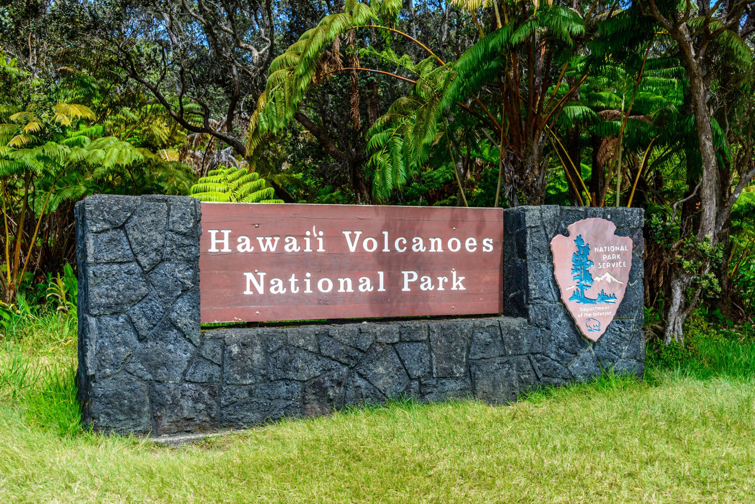 The Sign for Hawaii Volcanoes National Park in front of a vibrant green meadow.